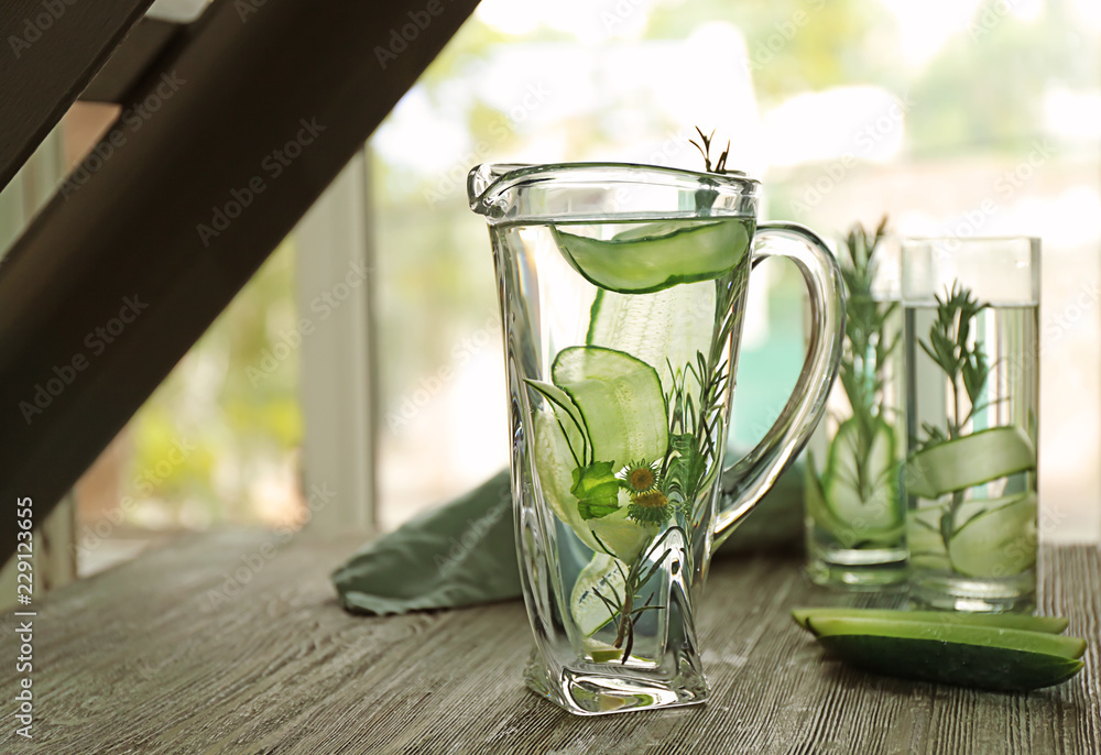 Jug of fresh cucumber water on wooden table