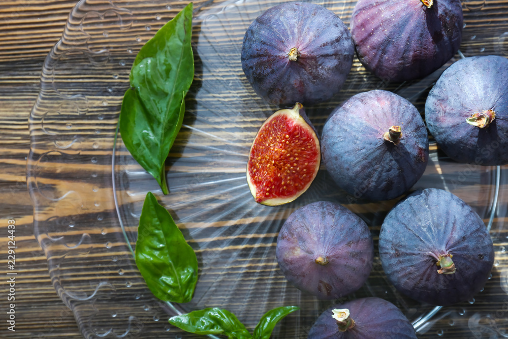 Plate with fresh ripe figs and basil on wooden table