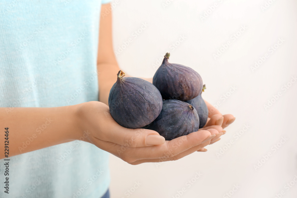 Woman holding fresh ripe figs on light background