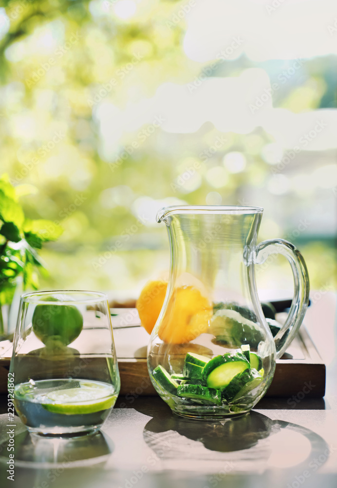 Glass of fresh cucumber water with jug on table
