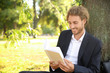 © Pixel-Shot - Handsome young businessman with book resting near tree in park