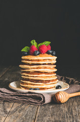 Wall Mural - Pancakes with berry fruits, honey and mint leaf on rustic wooden table. Vertical, copy space for text