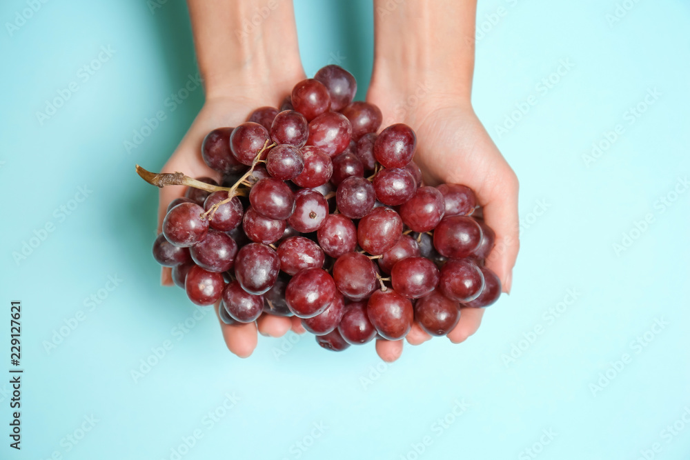 Female hands with ripe tasty grapes on color background