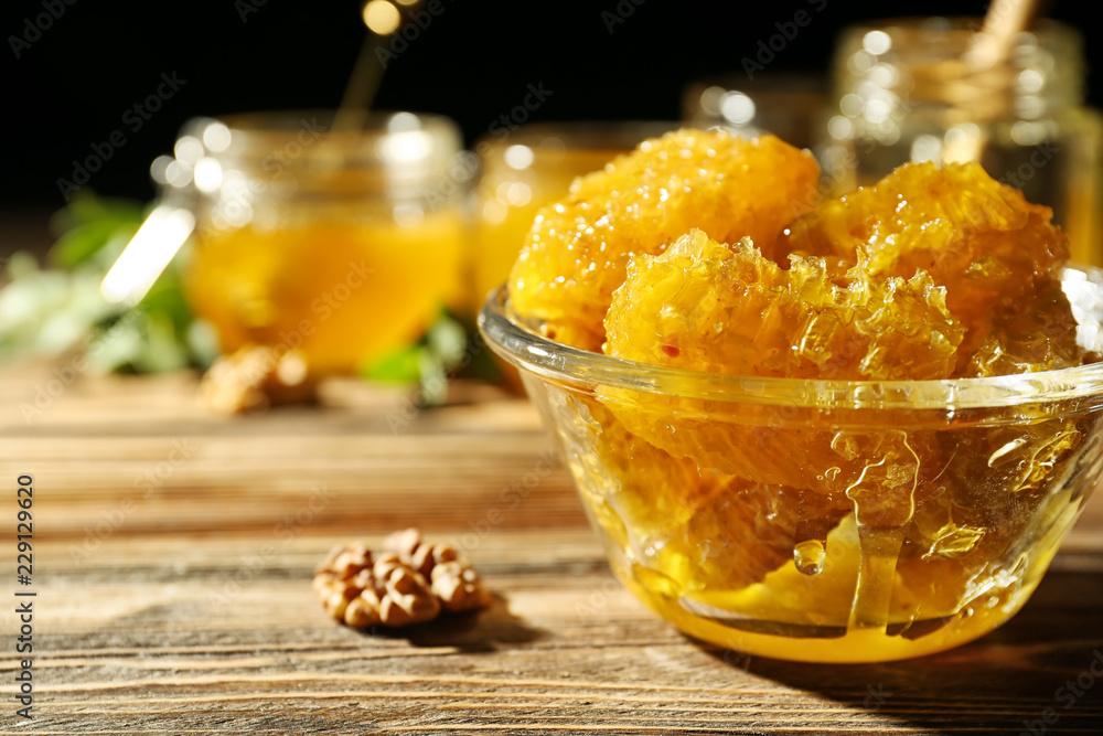 Bowl with sweet honeycomb and nut on wooden table, closeup