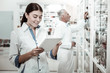 © Viacheslav Yakobchuk - Medicine range. Beautiful dark-haired pharmacist wearing white coat holding tablet while looking at medicine range