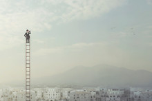 Businessman At The Top Of A Long Ladder Observes The City With His Binoculars