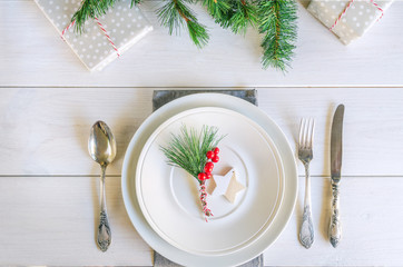 Wall Mural - Christmas table setting with traditional Christmas decoration in white red tone. Beautiful festive dinner background. Xmas tableware, plateб napkin and vintage cutlery, fir branch and red berries