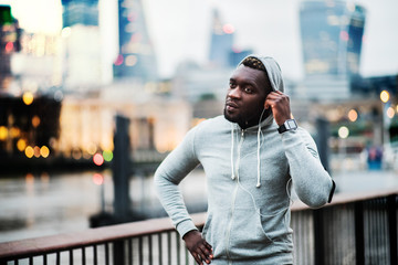 Wall Mural - Black man runner with smart watch and smartphone on the bridge in a city, resting.