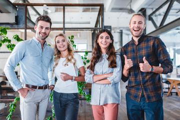 Wall Mural - happy young business team showing thumbs up and smiling at camera in office