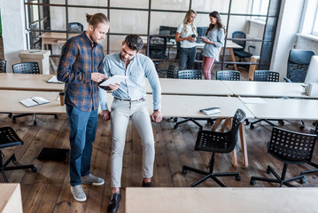 Wall Mural - high angle view of young male colleagues using digital tablet in office