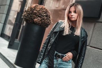 Fashion model woman in golf, blue jeans and black leather jacket posing outdoor. Street style 