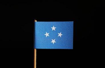 A national flag of Federated States of Micronesia on wooden stick on black background. The federation belongs to Oceania