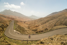 Panoramic View Of Winding Road With Cyclists At Sicasumbre, Fuerteventura, Spain.