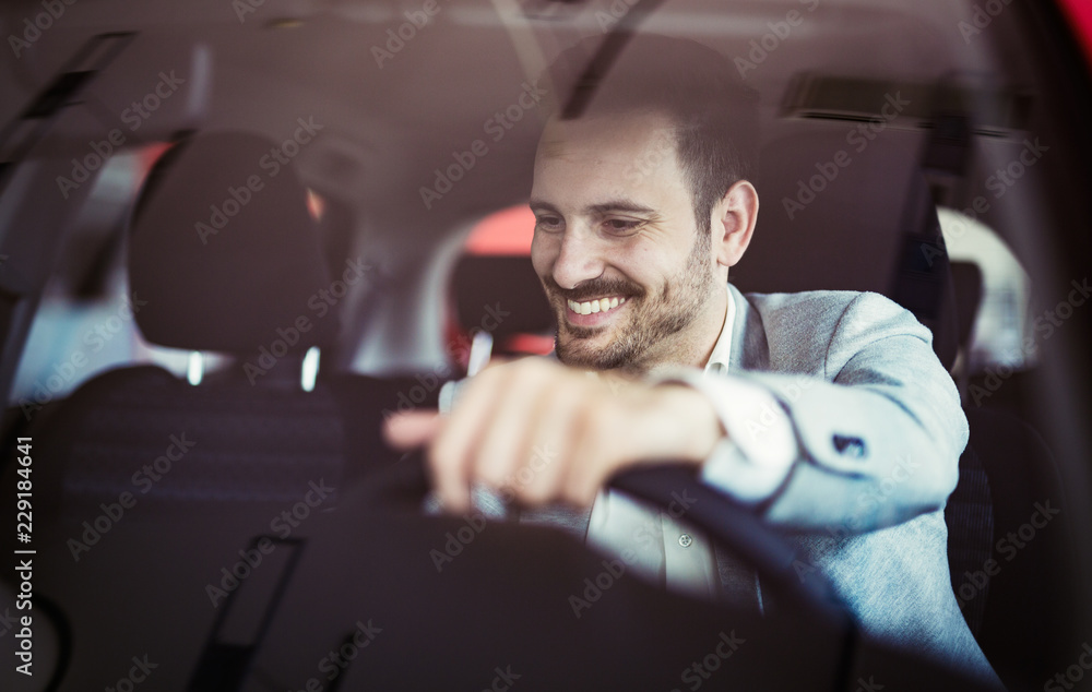 Attractive happy young man driving car and smiling - obrazy, fototapety, plakaty 