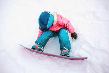 Snowboard Winter Sport. Little kid girl playing with snow wearing warm winter clothes. Winter background