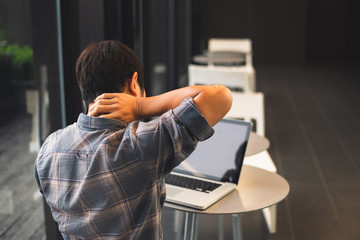 Back view Young man feeling hurt,fatigue, pain at neck, muscle during working with laptop in coffee shop cafe, stretching arms and body for relaxing, vintage tone, office syndrome concept,copy space.