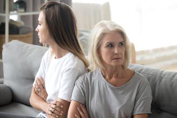 offended elderly mother and adult daughter sit back to back avoid talking or looking at each other, 
