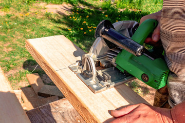 A man is sawing a board with a circular saw in the open air