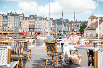 Young woman enjoying coffee sitting at the cafe outdoors near the harbour in Honfleur old town, France