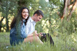 © soleg - young couple sitting on the grass in the forest and looking on sunset, listen to radio, summer nature, bright sunlight, shadows and green leaves, romantic feelings