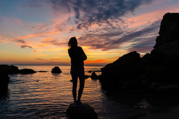 The silhouette of girl that standing on the stone near the sea