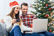 © baranq - Couple sitting on sofa and doing christmas shopping online with credit card and laptop