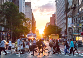 Crowds of people cross a busy intersection on 23rd Street and 6th Avenue in Manhattan with the colorful sunset in the background skyline