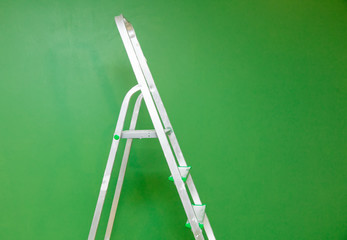 metal stepladder on a green background wall. Side view