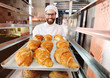 © Evgeniy Kalinovskiy - A young handsome male baker holds a tray with French croissants in front of a bakery and smiles.