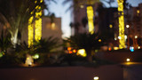 Fototapeta Londyn - Out of focus backdrop of downtown square with illuminated palms at dusk