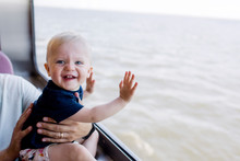 Laughing Baby Next To A Window Overlooking A Water View