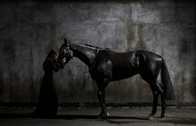 Side View Of Woman In Black Dress Standing With Horse In Dark Room