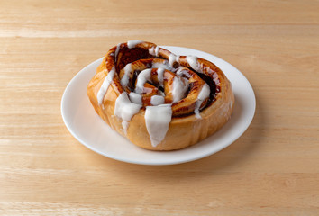 A freshly baked cinnamon roll on white plate atop a wood table.