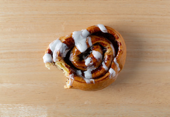 Wall Mural - Top view of a bitten cinnamon roll on a wood table.