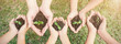© paulaphoto - Multicultural hands of adult and children holding young plant over green grass background. Earth day environment friendly harmony together spring concept banner.