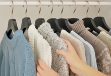 Autumn - Winter Fashion Concept. Woman Choosing Warm Knitwear On Hangers In Wardrobe.