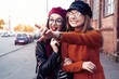 © opolja - Outdoors fashion portrait young pretty best girls friends in friendly hug. Walking at the city. Posing at the street. Wearing stylish outerwear and hats. Bright make up. Positive emotions.