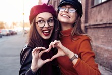 Outdoors Fashion Portrait Young Pretty Best Girls Friends In Friendly Hug. Walking At The City. Posing At The Street. Wearing Stylish Outerwear And Hats. Bright Make Up. Positive Emotions.