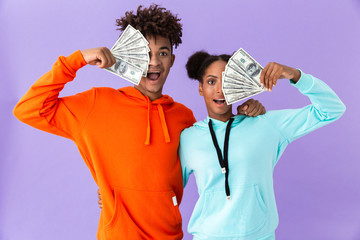 Poster - Photo of joyous african american couple in colorful clothes holding fans of dollars money, isolated over violet background