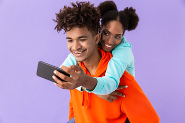 Sticker - Photo of beautiful african american woman taking selfie while hugging brother from back, isolated over violet background