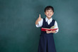 Leinwandbild Motiv Asian Chinese little Girl in uniform showing thumbs up against green blackboard