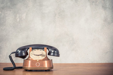 Fototapete - Retro antique classic outdated copper with black color rotary telephone from circa 1950s on wooden table front textured concrete wall background. Vintage instagram old style filtered photo