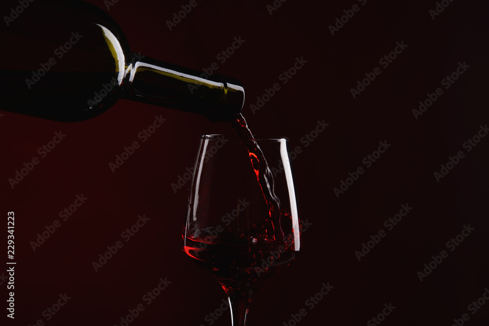 Pouring of red wine from bottle into glass on dark background
