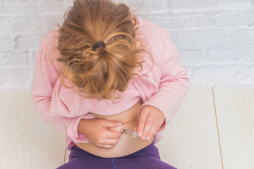 girl child is doing the insulin shot in the stomach on a background of white brick wall