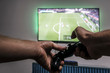 Man hold gamepad in hands in front of  tv screen with Pro Evolution Soccer. One gamer. Widescreen tv hanging on the wall