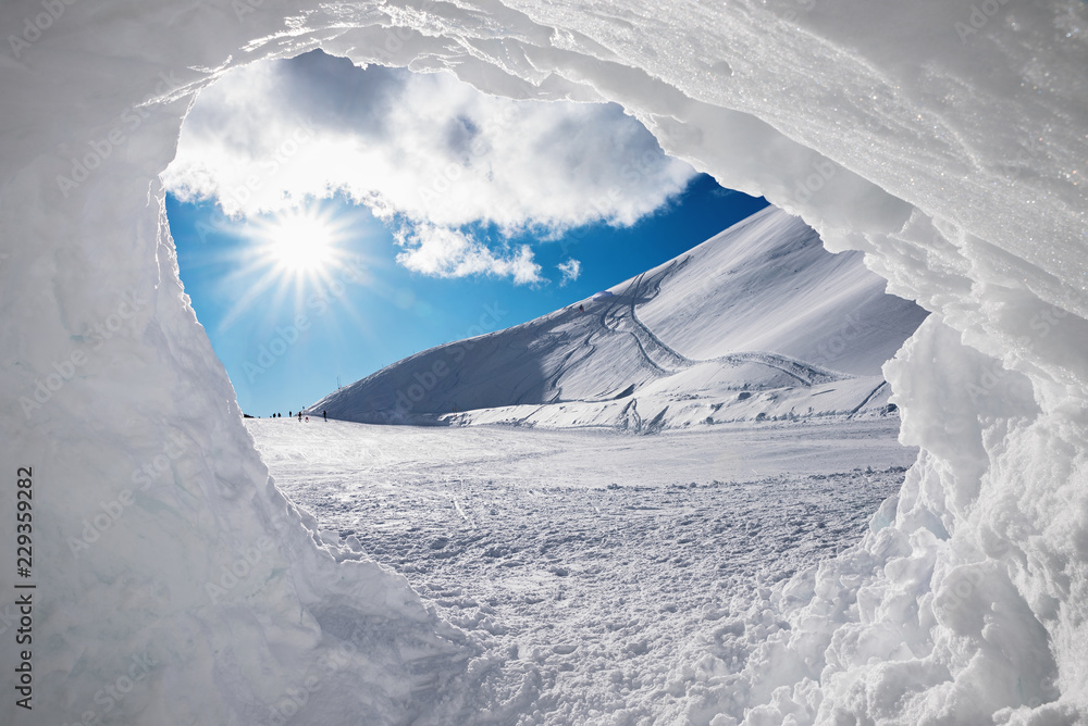 Blick aus der Schneehöhle auf verschneite Winterlandschaft mit Sonne - obrazy, fototapety, plakaty 