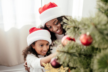 portrait of happy african american family in santa claus hats decorating christmas tree together at 