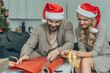© LIGHTFIELD STUDIOS - attractive young couple in santa hats decorating christmas gift together at home