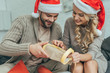 © LIGHTFIELD STUDIOS - creative young couple in santa hats decorating christmas gift together at home