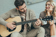 © LIGHTFIELD STUDIOS - handsome young man playing guitar for girlfriend at home while she sitting on couch with coffee